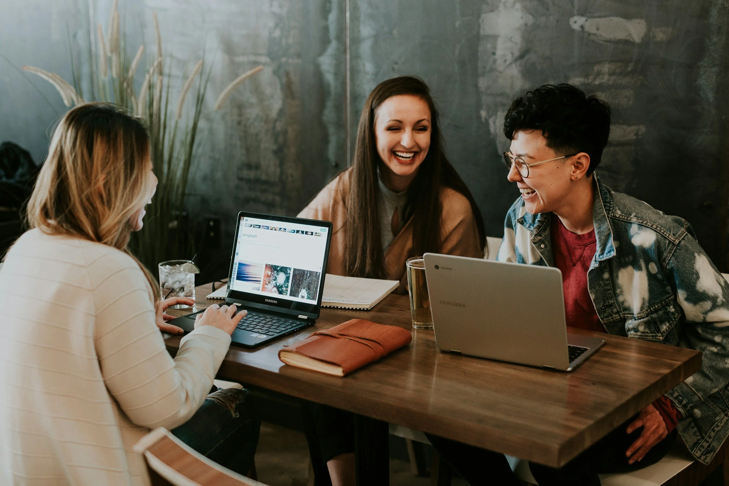 Tres mujeres riendo y compartiendo una reunión de trabajo alrededor de una mesa con laptops